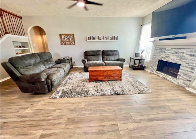 living room featuring a ceiling fan, wood finished floors, a textured ceiling, arched walkways, and a fireplace