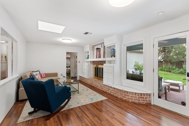 living area with wood finished floors, a skylight, a brick fireplace, and ornamental molding