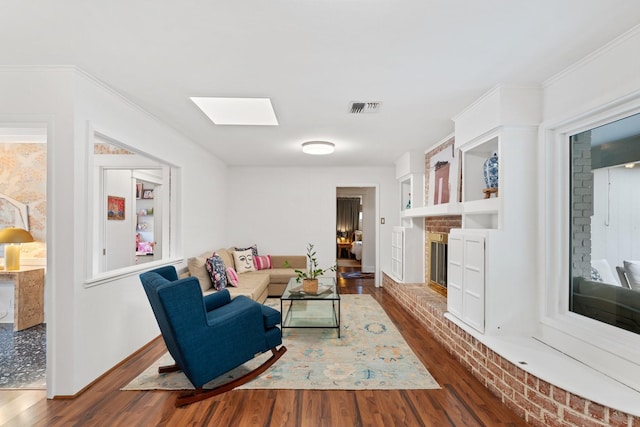 living area featuring wood finished floors, a brick fireplace, a skylight, baseboards, and ornamental molding