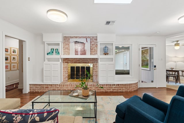 living room with wood finished floors, ceiling fan, ornamental molding, and a brick fireplace