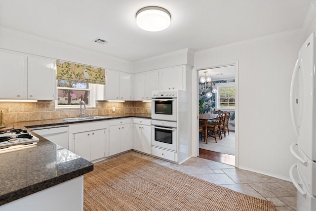 kitchen with white appliances, a sink, crown molding, decorative backsplash, and white cabinetry