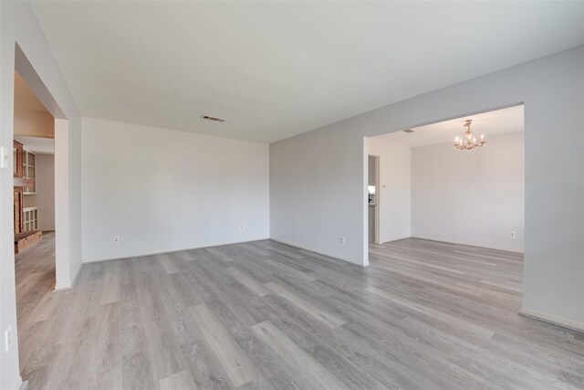 empty room with light wood-style flooring, a chandelier, and baseboards