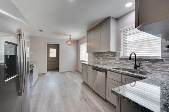 kitchen with appliances with stainless steel finishes, a sink, gray cabinets, decorative backsplash, and light stone countertops