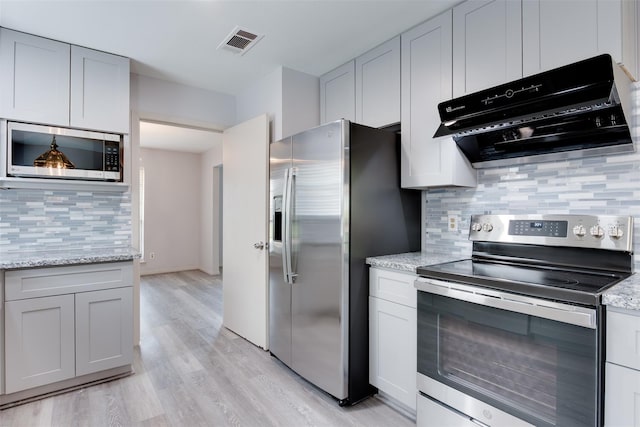 kitchen featuring stainless steel appliances, extractor fan, tasteful backsplash, light wood-type flooring, and light stone countertops