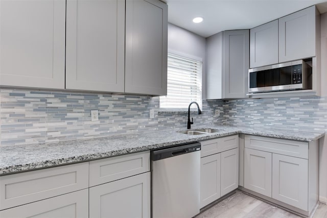 kitchen featuring stainless steel appliances, a sink, light wood-type flooring, and light stone countertops