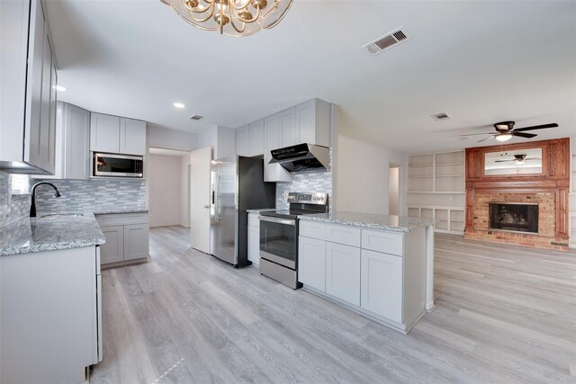 kitchen featuring appliances with stainless steel finishes, under cabinet range hood, a sink, light wood finished floors, and a brick fireplace