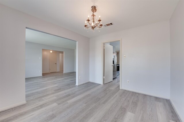spare room with a chandelier, light wood finished floors, and baseboards