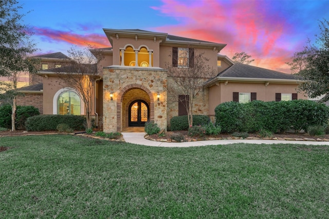 mediterranean / spanish house with stucco siding, a lawn, stone siding, and french doors