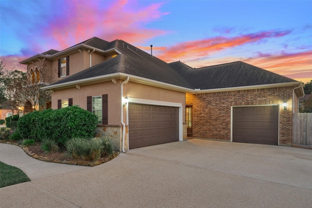 view of front facade featuring an attached garage, concrete driveway, stucco siding, and roof with shingles