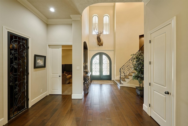 entryway with a towering ceiling, french doors, stairs, dark wood-type flooring, and ornamental molding