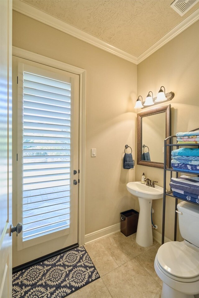 half bath featuring toilet, tile patterned flooring, ornamental molding, baseboards, and a textured ceiling