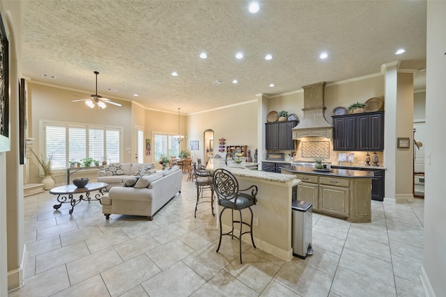 kitchen featuring a kitchen island with sink, crown molding, open floor plan, a ceiling fan, and a kitchen bar