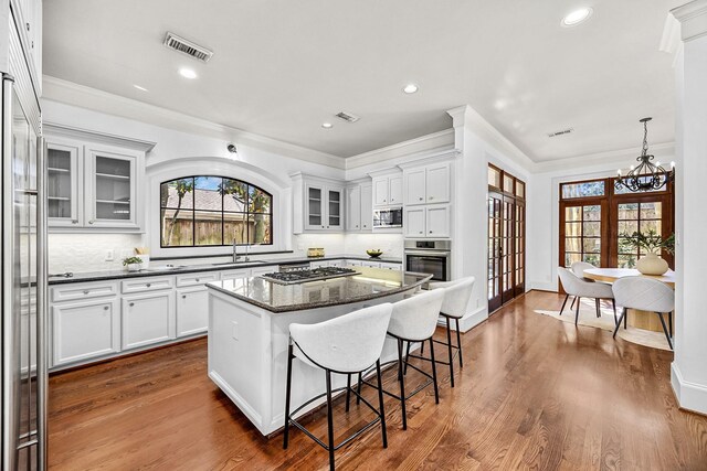 5105 Pocahontas St, Bellaire, TX 77401 - kitchen featuring a kitchen breakfast bar, stainless steel appliances, decorative backsplash, white cabinetry, and crown molding