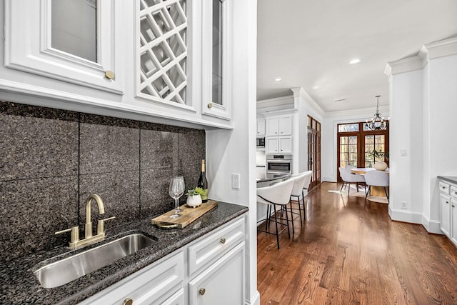 5105 Pocahontas St, Bellaire, TX 77401 - kitchen with tasteful backsplash, ornamental molding, a chandelier, white cabinets, and dark wood-style flooring