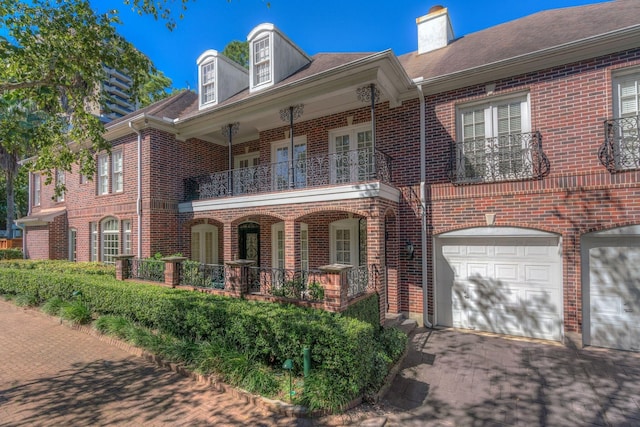 view of front facade with a balcony, brick siding, a porch, a chimney, and driveway