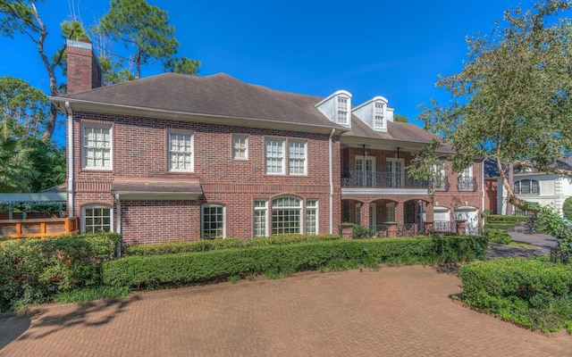 georgian-style home featuring brick siding, a balcony, and a chimney