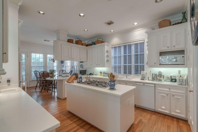 kitchen featuring white appliances, crown molding, a kitchen island, white cabinetry, and light countertops