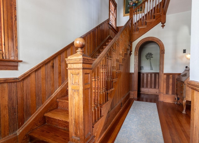 stairs featuring a wainscoted wall, wooden walls, wood finished floors, and a high ceiling