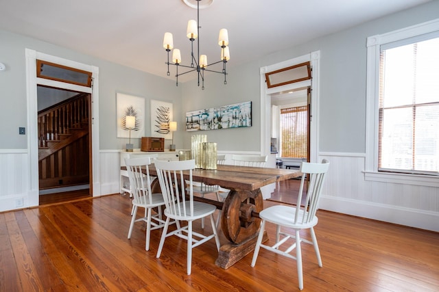 dining room featuring a wainscoted wall, wood-type flooring, a chandelier, and stairway