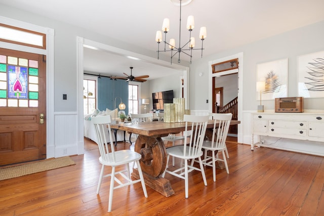 dining room with a chandelier, wainscoting, wood finished floors, a decorative wall, and ceiling fan