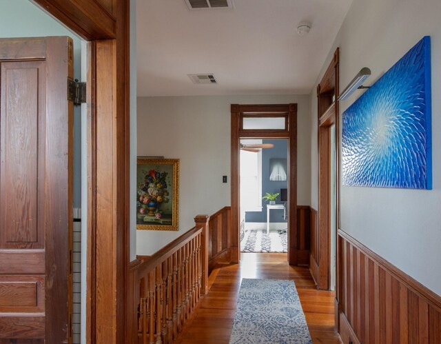 corridor with wainscoting, wood finished floors, and wood walls