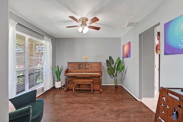 living area with a ceiling fan, wood finished floors, a textured ceiling, and baseboards