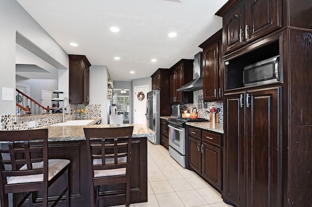 kitchen featuring wall chimney exhaust hood, appliances with stainless steel finishes, backsplash, dark brown cabinets, and recessed lighting