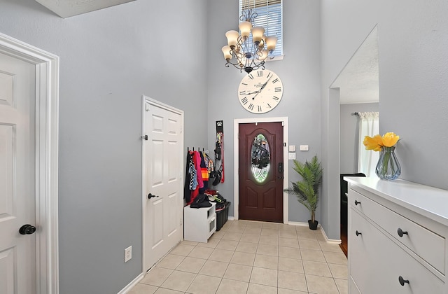 entryway featuring a high ceiling, light tile patterned floors, a chandelier, and baseboards
