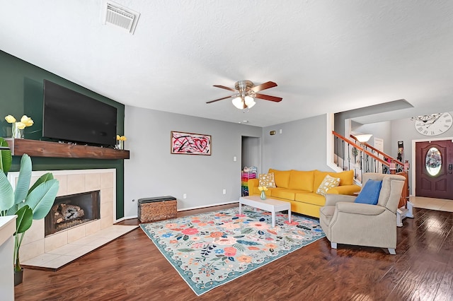 living room with stairs, ceiling fan, wood finished floors, a tiled fireplace, and baseboards