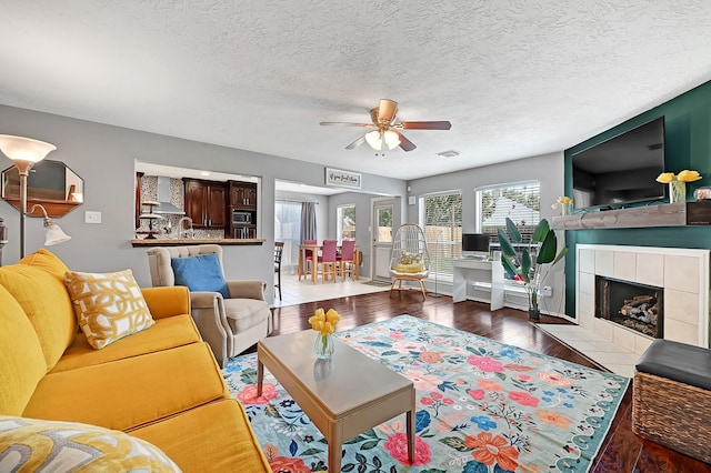 living room featuring hardwood / wood-style flooring, ceiling fan, a fireplace, and a textured ceiling