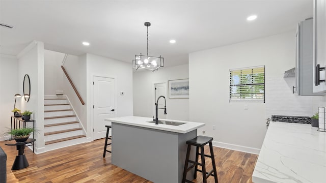kitchen with a sink, a kitchen breakfast bar, wood finished floors, a center island with sink, and recessed lighting