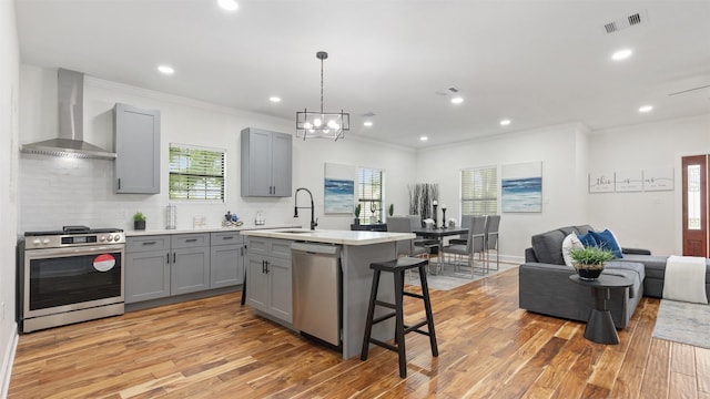 kitchen with gray cabinets, wall chimney range hood, appliances with stainless steel finishes, light countertops, and light wood finished floors