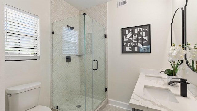 bathroom featuring toilet, a shower stall, double vanity, and baseboards