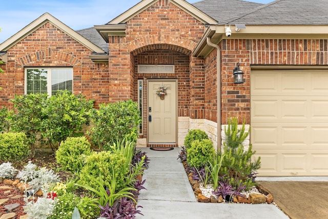 entrance to property featuring an attached garage, brick siding, and a shingled roof