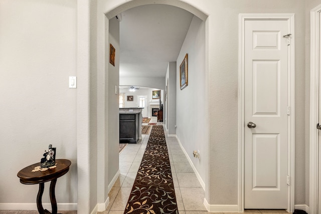hallway with arched walkways, light tile patterned flooring, and baseboards