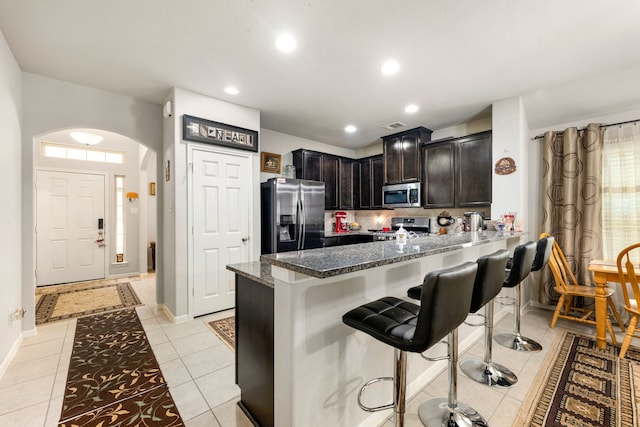 kitchen with appliances with stainless steel finishes, arched walkways, a breakfast bar, dark stone countertops, and decorative backsplash