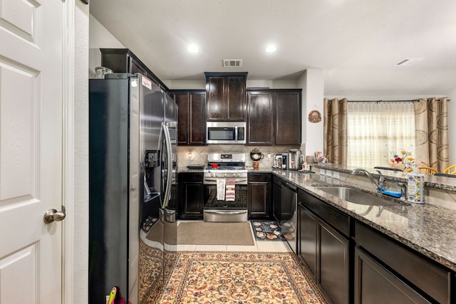 kitchen with stainless steel appliances, a sink, backsplash, dark brown cabinets, and light tile patterned flooring