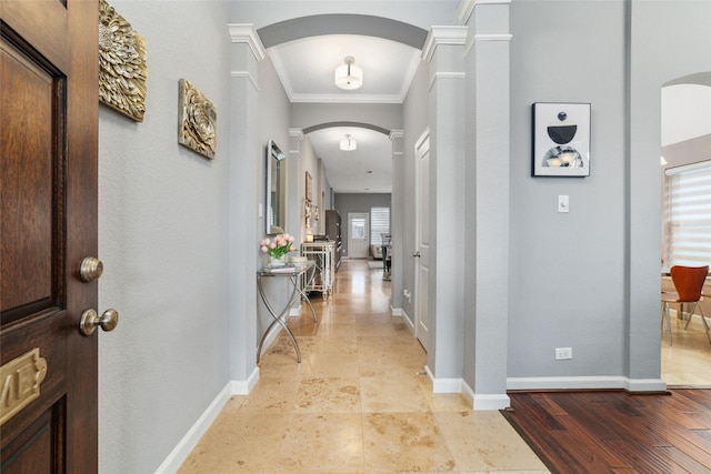 hallway featuring arched walkways, crown molding, baseboards, and ornate columns