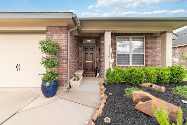 view of exterior entry with brick siding, a garage, and driveway