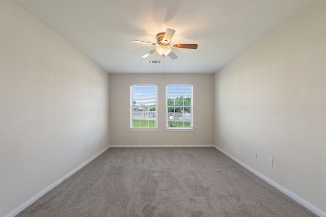empty room with light colored carpet, a ceiling fan, baseboards, and a textured ceiling