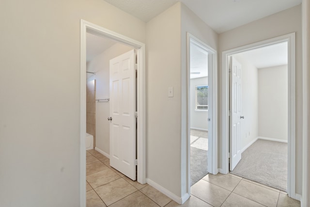 hall featuring light tile patterned floors, baseboards, and light carpet