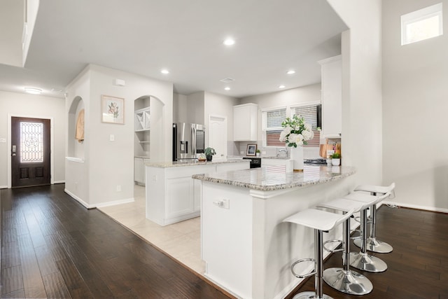 11707 Finnick Bend Dr, Tomball, TX 77377 - kitchen featuring stainless steel fridge with ice dispenser, arched walkways, a peninsula, light wood-style floors, and recessed lighting