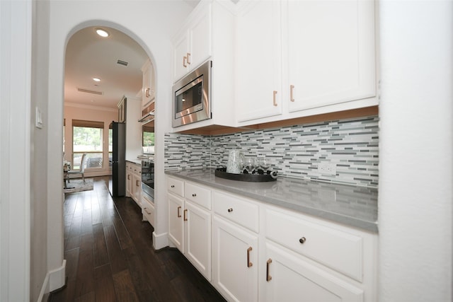 5502 Charlton Ridge Ln, Fulshear, TX 77441 - kitchen featuring stainless steel microwave, decorative backsplash, crown molding, white cabinetry, and dark wood-type flooring