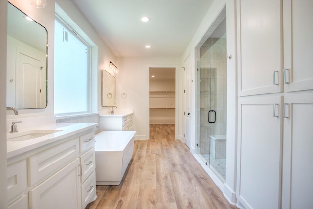1973 Greentree Dr, Huntsville, TX 77340 - bathroom featuring a stall shower, two vanities, wood finished floors, a tub, and recessed lighting