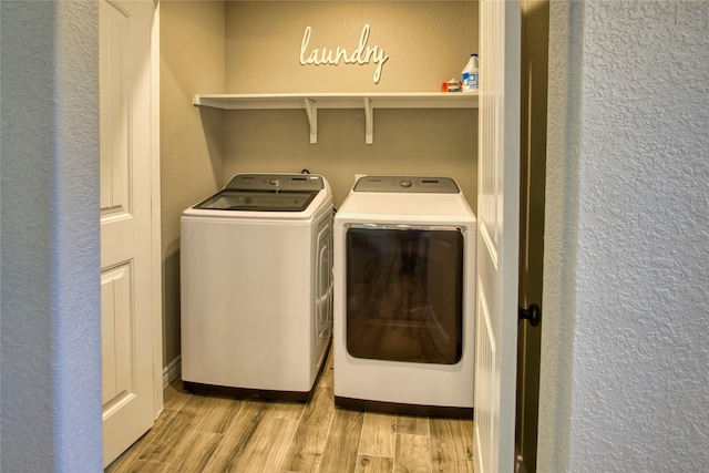 laundry room with independent washer and dryer, light wood-type flooring, and a textured wall