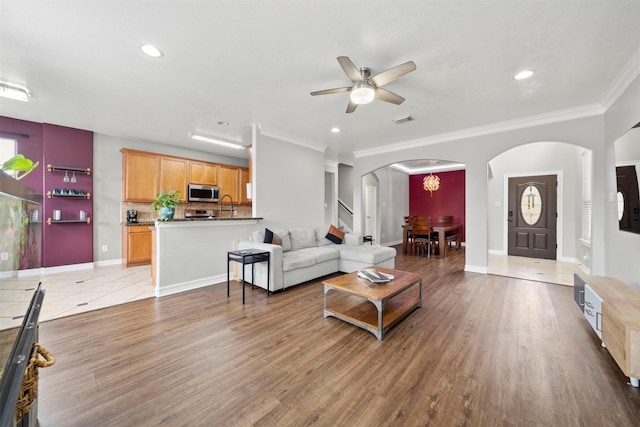 living room featuring arched walkways, a ceiling fan, light wood-style floors, baseboards, and recessed lighting