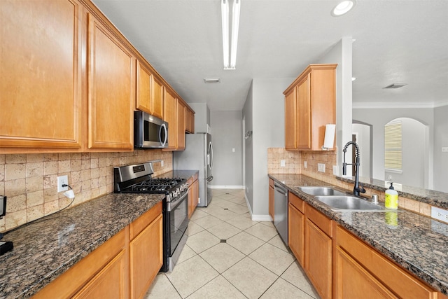 kitchen with appliances with stainless steel finishes, a sink, arched walkways, light tile patterned floors, and decorative backsplash