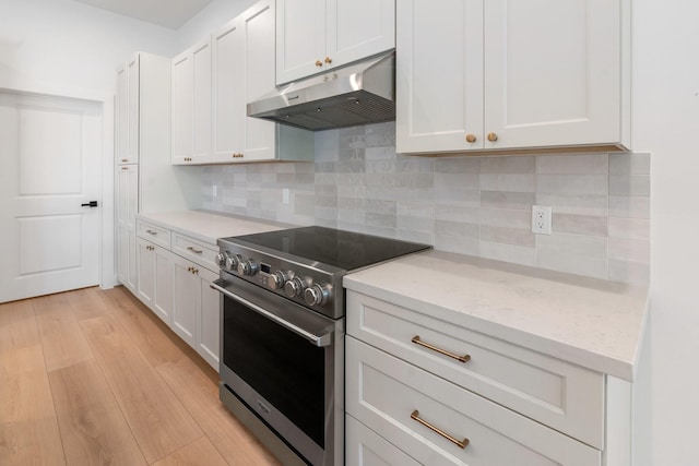 kitchen featuring under cabinet range hood, high end stainless steel range, light wood finished floors, tasteful backsplash, and white cabinetry