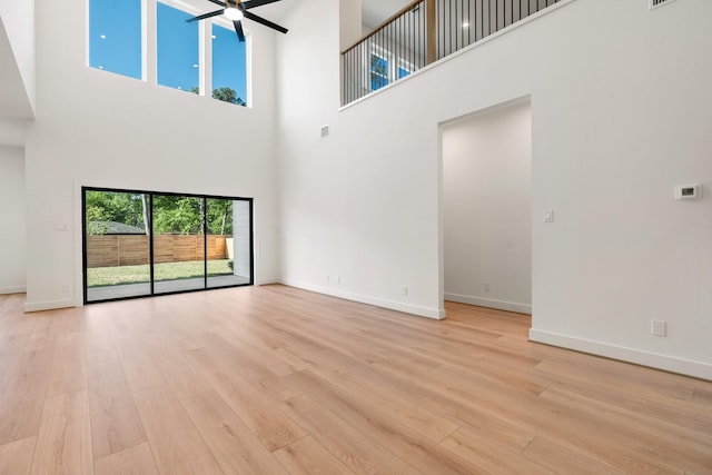 unfurnished living room featuring a towering ceiling, ceiling fan, light wood-type flooring, and baseboards
