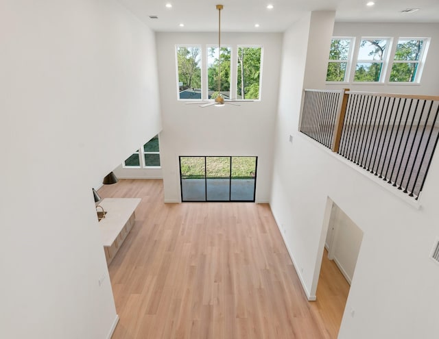 unfurnished living room with light wood-style floors, ceiling fan, recessed lighting, a towering ceiling, and baseboards